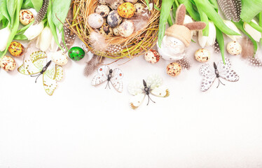 Spring Easter holiday white background with tulips, quail eggs, butterflies, bunny and feathers in a nest. Banner with copy space. Top view