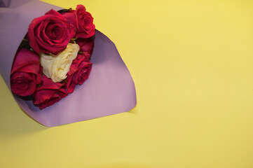 Bouquet of red roses in purple packaging lies on a yellow background