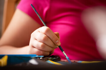 Child artist paints with a brush and tempera colors