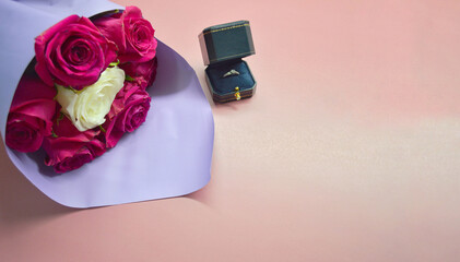 Bouquet of red roses in purple package and box with ring on pink background