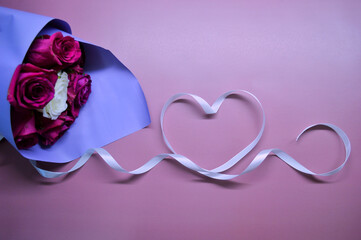 Bouquet of red roses in purple packaging lies on pink background