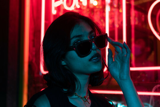 Sillhoutte of hip-hop girl in cap at the neon light. Fashion portrait of modern young woman in cap and sunglasses.