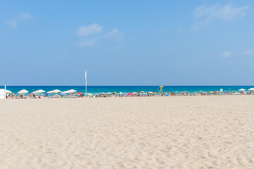 large beach with sunbathers on the shore under colored umbrellas