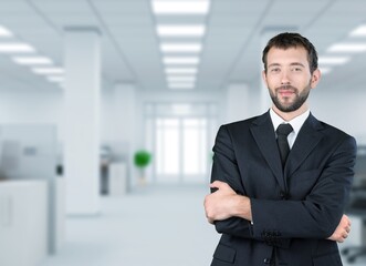 Obraz premium Smiling young businessman with arms crossed in office background