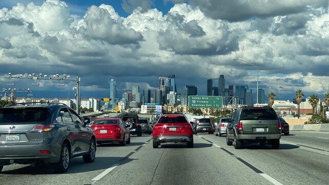 LOS ANGELES, CA, MAR 2021: freeway with cars driving towards downtown skyscrapers and tall buildings in the distance, overcast day with clouds overhead