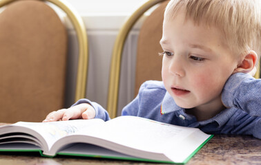 close-up of a pensive blond-haired toddler leaning over a book holding his head