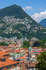 Naklejka na ściany i meble View of Old Town Lugano, Switzerland. The scenic cityscape and red rooftops of Lugano -- Cathedral of Saint Lawrence bell tower in the foreground