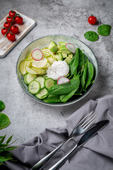 Poached Egg. Green salad with avocado, cucumber, spinach leaves, zucchini and radishes in a plate on a gray stone table. Restaurant Menu