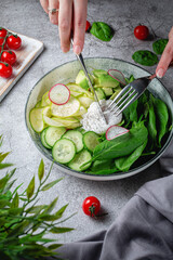 Woman's hands cut a poached egg. Green salad with avocado, cucumber, spinach leaves, zucchini and radishes on a gray stone table. Restaurant Menu