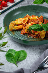 Italian pasta Conchiglioni Rigati stuffed with dry tomatoes and meat with basil and cheese on a gray stone table. Restaurant Menu