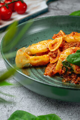 Italian pasta Conchiglioni Rigati stuffed with dry tomatoes and meat with basil and cheese on a gray stone table. Restaurant Menu