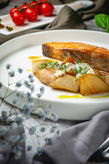 Salmon fillet baked with rustic potatoes on sweet pears stuffed with noble cheese with a sauce of ripe oranges in a plate on a gray stone table. Restaurant Menu