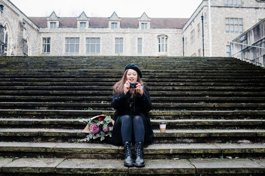 Asian woman sat on steps taking pictures in Winchester, UK