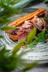 Homemade beef meat sandwich in croissant with lettuce, tomato and arugula leaves in a plate on a gray stone table. Restaurant Menu