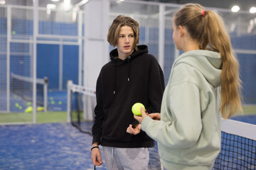 Teenagers chat with each other after playing padel on the tennis court