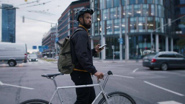 Young African-american man commuter with bicycle crossing the road in city.