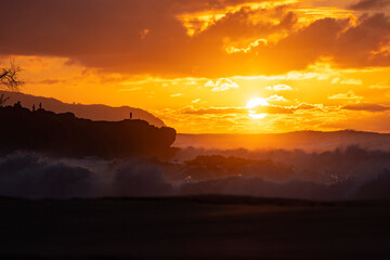 Perfect warm summer sunset at the beach with big waves and clouds with a silhouette of a man staying on the cliff