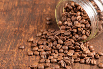 Coffee beans falling out of a glass pot on rustic wood, selective focus.