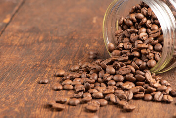 Coffee beans falling out of a glass pot on rustic wood, selective focus.