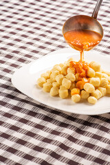 Potato gnocchi with sauce on a white plate on a black and white checkered tablecloth, selective focus.