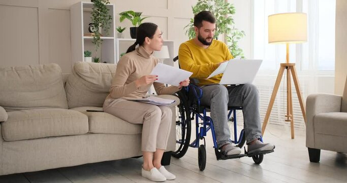 Handicapped man with wife analyzing documents while using laptop at home