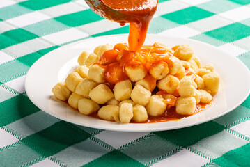 Potato gnocchi with sauce in detail on a white plate on a green and white checkered tablecloth, selective focus.