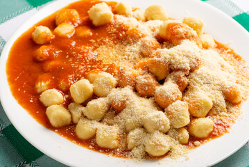 Potato gnocchi with sauce and grated cheese in detail on a white plate on a green and white checkered tablecloth, selective focus.
