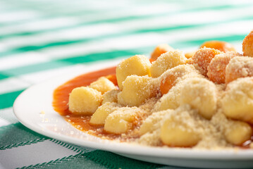 Potato gnocchi with sauce and grated cheese in detail on a white plate on a green and white checkered tablecloth, selective focus.