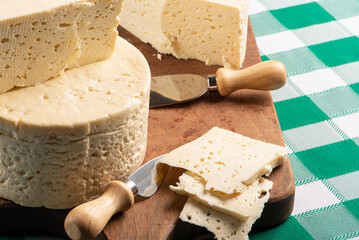 Semi-cured cheese from Brazil arranged on a rustic board on a green and white checkered tablecloth, selective focus.