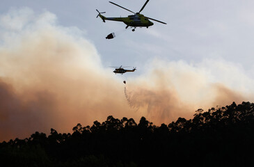 Fototapeta na wymiar The silhouette of two firefighting helicopters flying during a forest fire