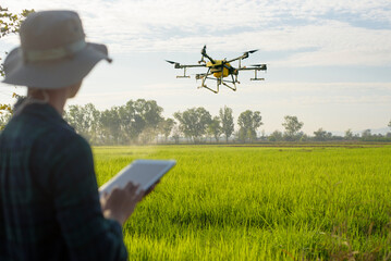 Young smart farmer controlling drone spraying fertilizer and pesticide over farmland,High technology innovations and smart farming
