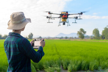 Young smart farmer controlling drone spraying fertilizer and pesticide over farmland,High technology innovations and smart farming