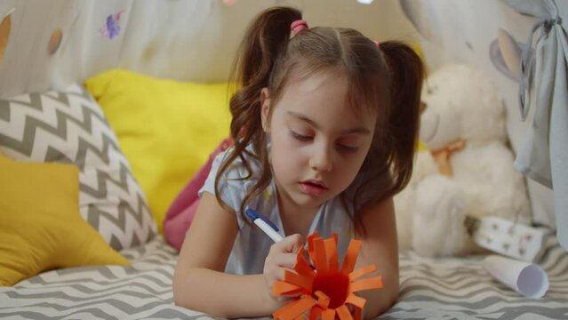 Cheerful cute little girl makes a space alien lying in a tent. Game of space aliens and astronauts spending time on vacation at home. 