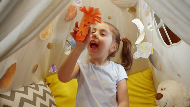 Happy little girl is playing with a paper space alien sitting in a tent at home. Preschool girl plays with a paper humanoid in capturing planets, an ALIEN FLIES BETWEEN PLANETS