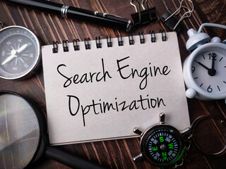 Top view compass,clock,magnifying glass,pen and notebook with text Search Engine Optimization on wooden background.