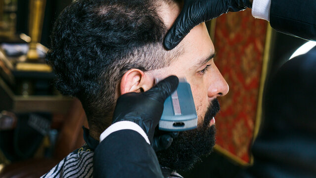 Horizontal photo of a man in profile in a barber shop, using a hair clipper.
Lifestyle. 