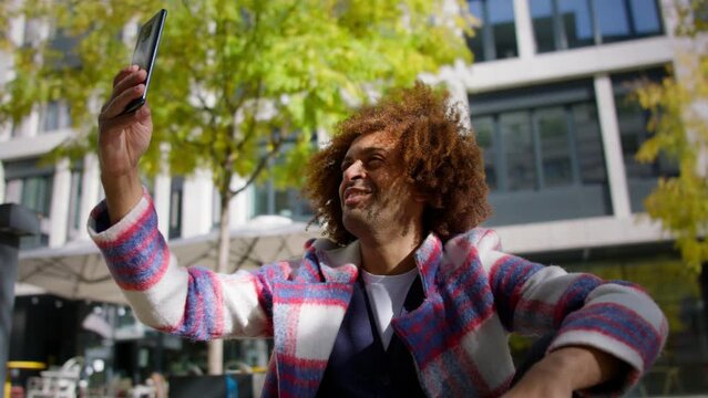 Low angle view of cool multiracial mid audlt man having vide call with smartphone outdoors in town
