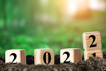 Changing year concept in wooden blocks cubes with growing plant at sunrise.
