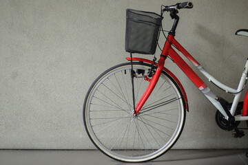 Close-up of bicycle front wheel with basket in front of gray wall with copy space - Powered by Adobe