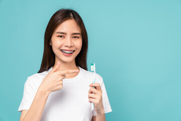 Smiling Asian woman holding toothbrush with braces on teeth isolated on blue background, Concept oral hygiene and health care.