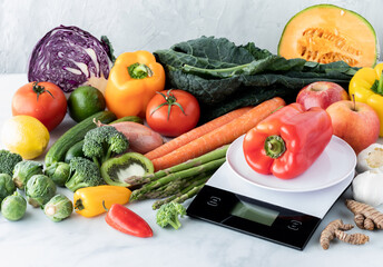 Abundance of produce with a food scale in front and a red pepper on top.