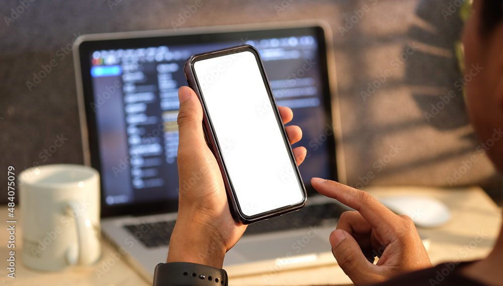 Poster man sitting in front of computer laptop and holding smart phone with white screen.