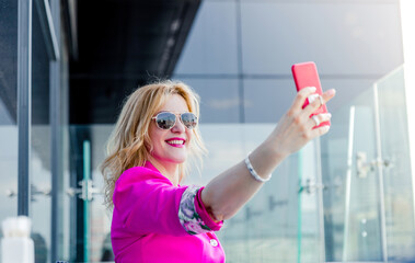 A successful woman entrepreneur in a magenta jacket makes a selfie on the terrace of a cafe in a business center.