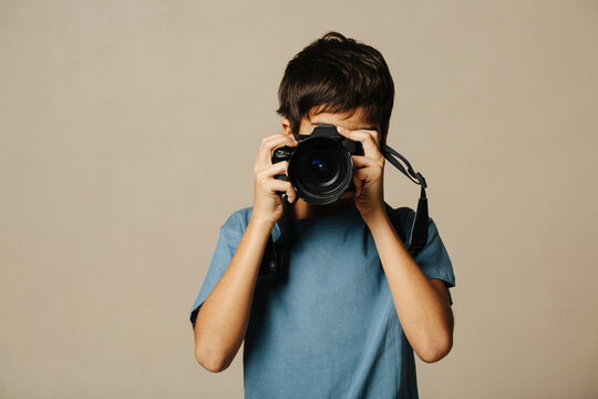 Indian boy taking a photo with a digital camera over beige background.