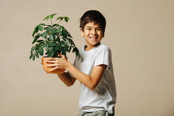 Joyous casually dressed indian boy holding a potted plant in his arms