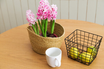 On a wooden table are a vase with hyacinth, lemons in a metal basket and a white cup. Home comfort concept