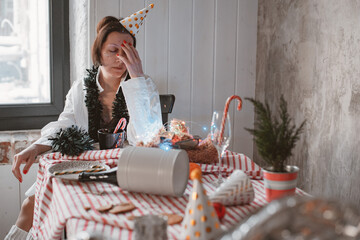Tired woman in party hat with hangover and headache after celebrating new year eve at home