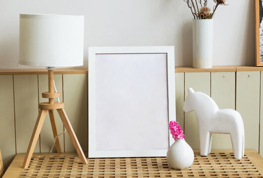 Elegant composition at living room interior with wooden chest of drawers, white mock up poster frame, spring flowers, decoration, lamp and stylish presonal accessories in modern home decor.