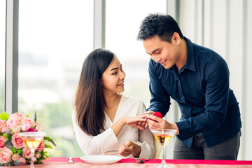 Young handsome romantic asian man giving diamond ring for surprise to girlfriend and talking together in valentine day at the restaurant