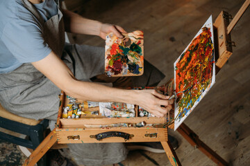 Painter working in real studio with oil paints and brushes, creating canvas, modern art. Young man with palette closeup